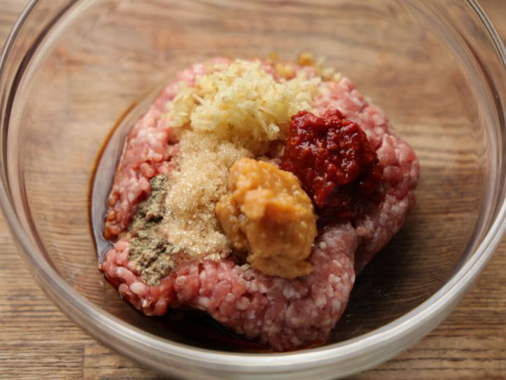透明なボウルに豚ひき肉、みじん切りしょうが、砂糖、味噌、豆板醤などの調味料が入っている。