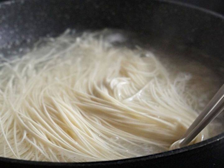 黒い鍋でそうめんが茹でられており、箸で麺をほぐしている様子。
