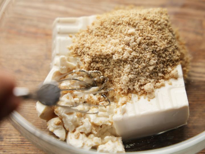 透明なボウルに入った絹ごし豆腐とすり白ごまを泡だて器で混ぜ始めている。