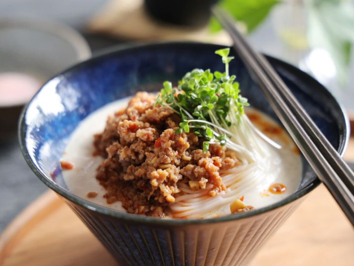 青い器に盛られた冷やし坦々そうめん。白いスープにひき肉とブロッコリースプラウトが乗っている。