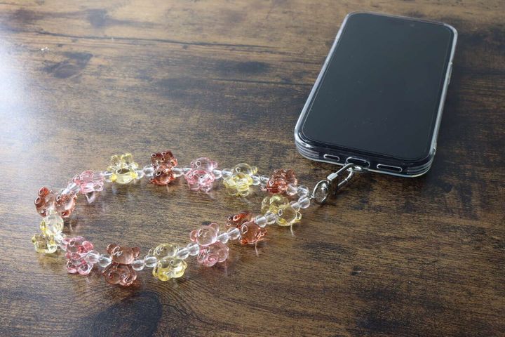 木目のテーブルに置かれたスマホとクマ型ビーズストラップ