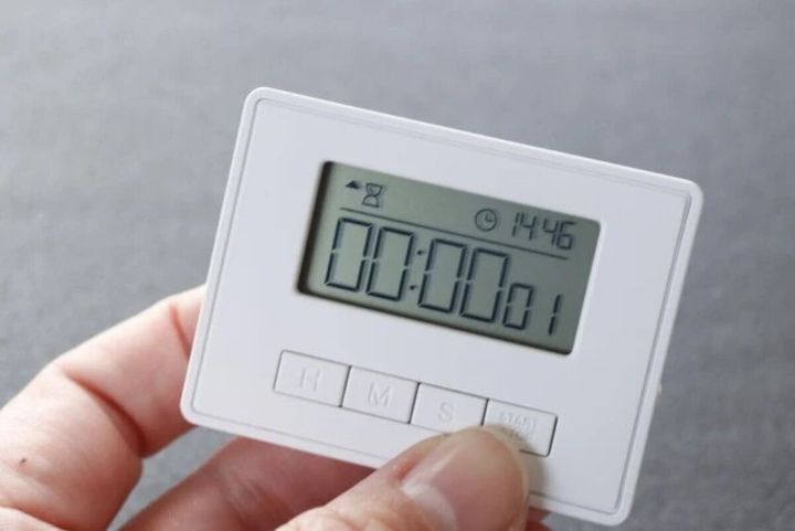白いキッチンタイマーのボタンを指で押している手元