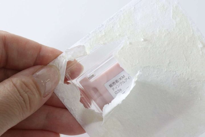 手がアイシャドウのパッケージ台紙を破り、中の商品が見えている様子