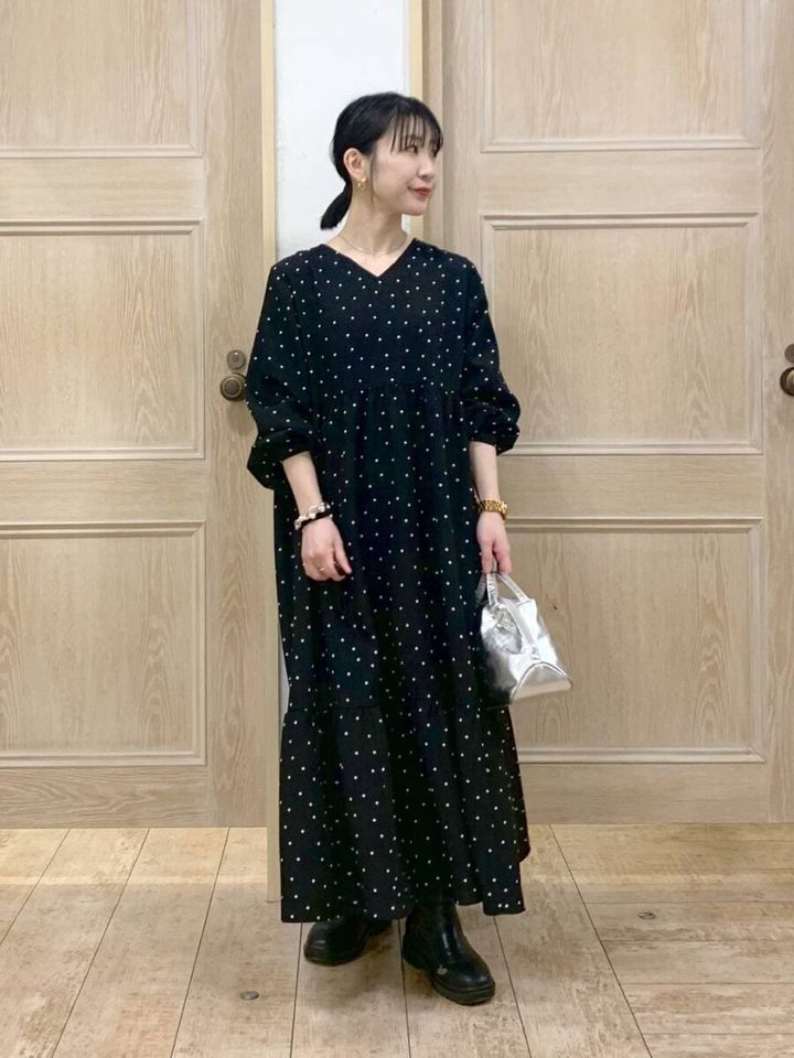 黒のドット柄ワンピースを着てシルバーバッグを持つ女性