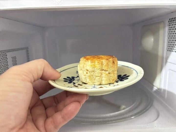 植物柄の小皿にのせたスコーンを電子レンジに入れようとしている手