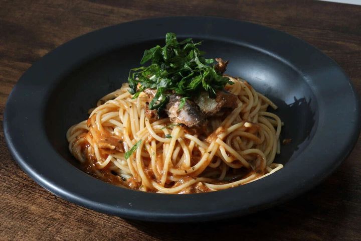 黒い皿に盛られた、大葉が乗ったいわしトマト煮パスタのアップ