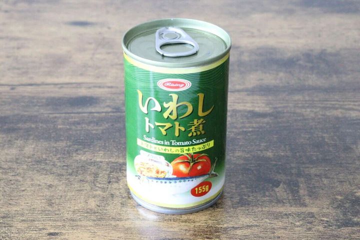 緑色の「いわしトマト煮」缶詰が木目のテーブルに置かれている
