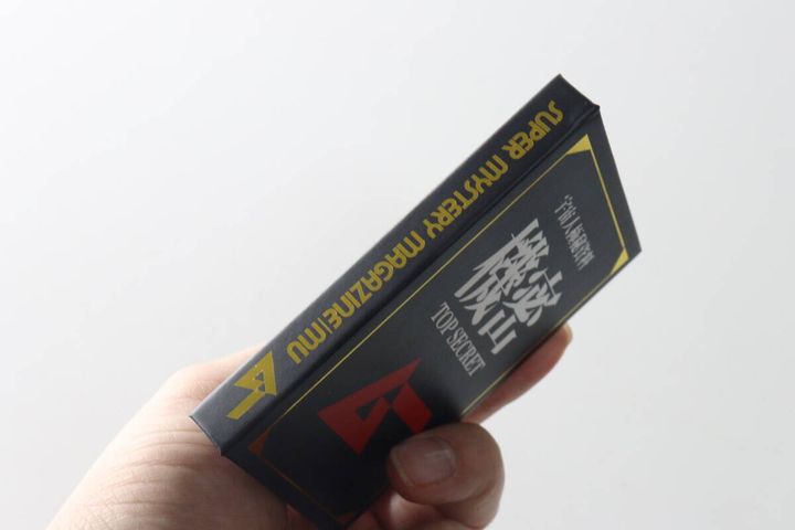 手に持ったブック型メモ帳の背表紙。SUPER MYSTERY MAGAZINE MUの文字