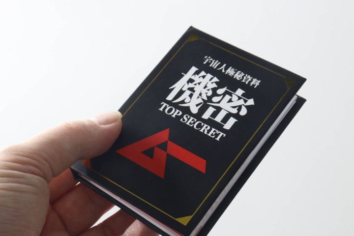 手に持った「宇宙人極秘資料 機密 TOP SECRET」と書かれた黒いブック型メモ帳