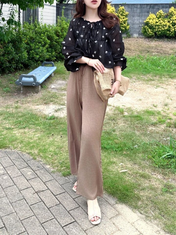 花柄シアー黒ブラウスとブラウンのワイドパンツを合わせた女性