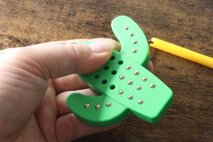 手でサボテン型キーホルダーを握り、吸着した鉄球を指で押し戻している様子