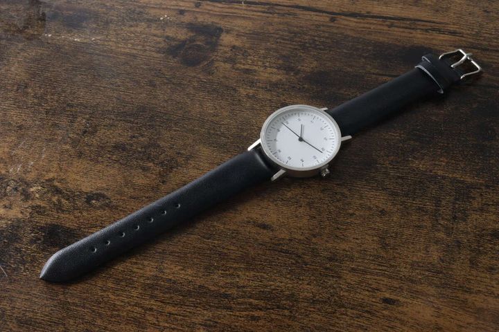 木目調のテーブルに置かれた黒いベルトのシンプルウォッチ
