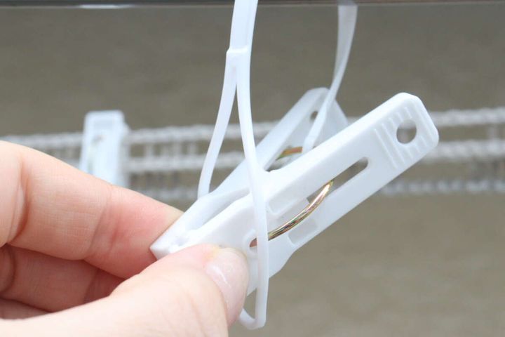 手が白い洗濯ピンチのひもを物干し竿に引っ掛けている