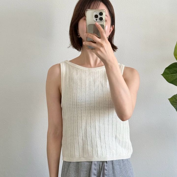 白いニットタンクトップを着た女性がスマホで顔を隠している