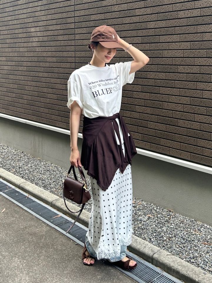 白のロゴTにドット柄スカートとデニムを重ね、茶色のキャップを被る女性