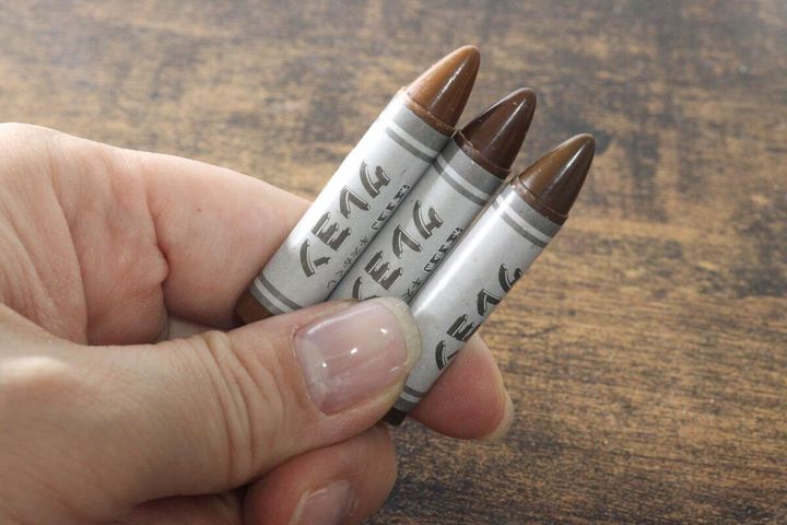 指でつまんだダークブラウン系のキズかくしクレヨン3本