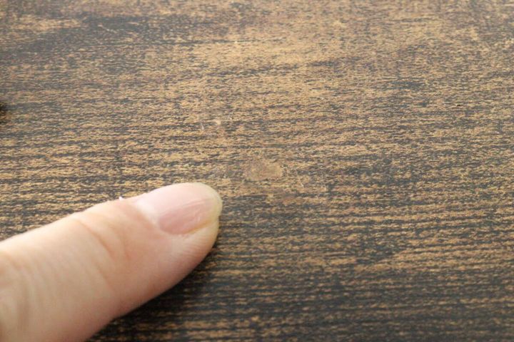クレヨンで補修された木目調のテーブルのキズ跡を指で指し示している
