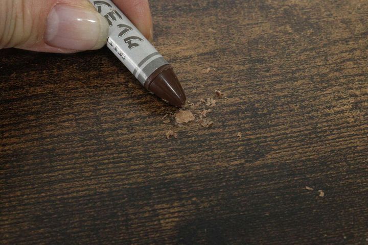 木目調のテーブルのキズにダークブラウンのクレヨンをすり込んでいる