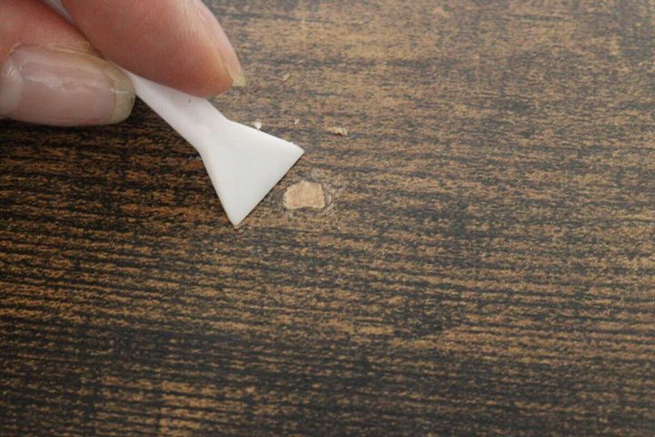 木目調のテーブルのキズ部分から白いヘラで余分なクレヨンを削り取っている