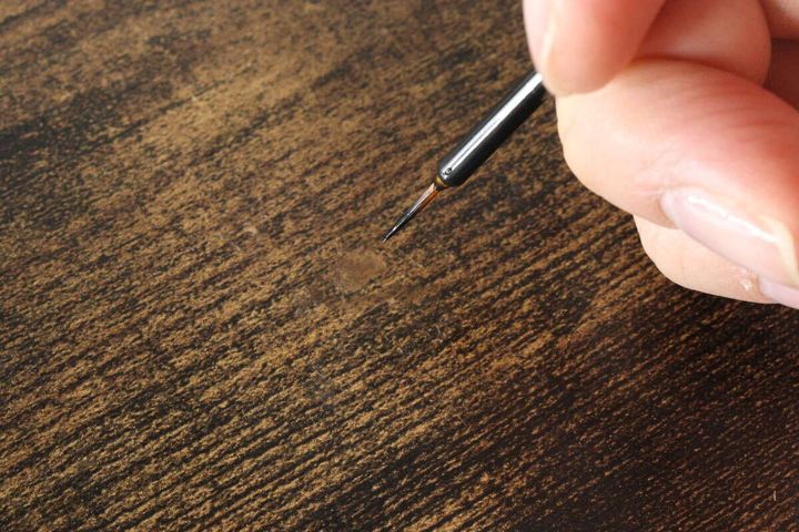 木目調のテーブルの補修箇所に細い筆で木目を描き足している