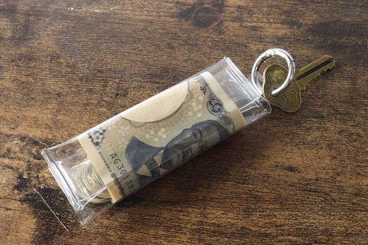 PVCコインポーチに硬貨と千円札、鍵がリングに取り付けられて木目のテーブルに置かれている