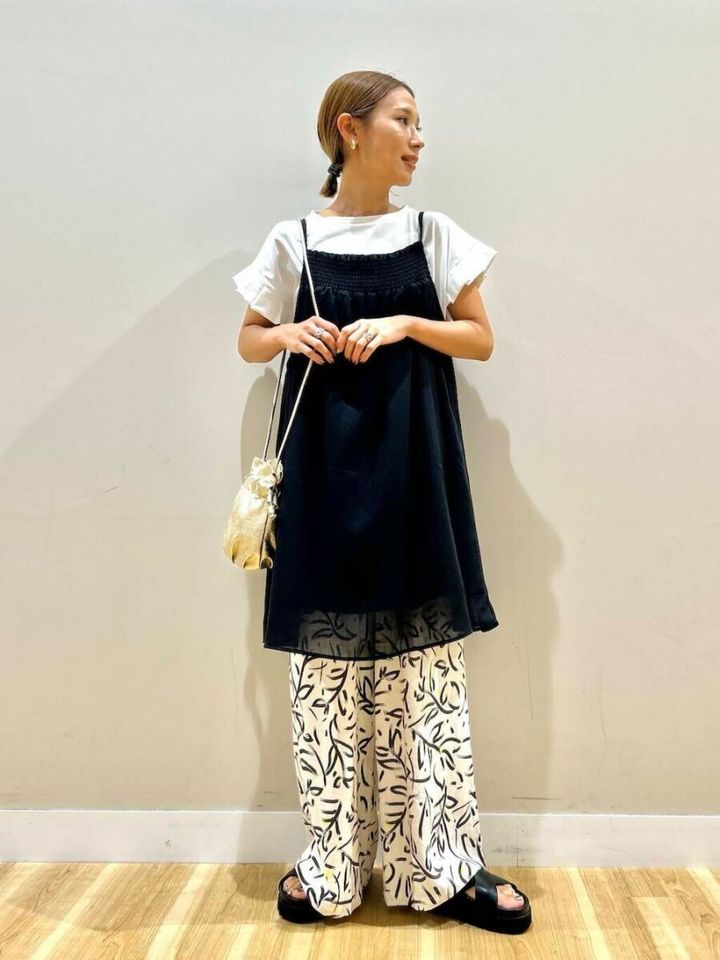 白Tシャツに黒キャミチュニックと柄パンツを重ね着し、巾着バッグを持つ女性