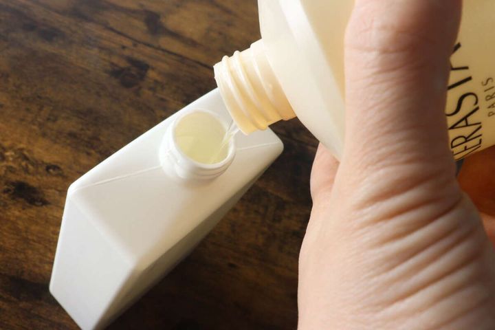 白いポンプボトルの小さな注ぎ口に、別のボトルから液体を詰め替えている