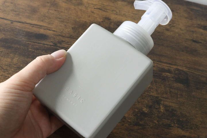 女性の手がグレーの泡ポンプボトルを持ち、上から斜めに撮影されている