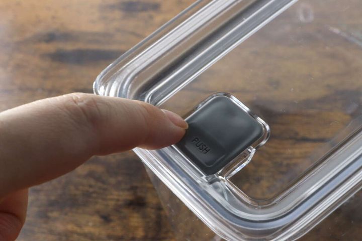 人差し指で密閉容器のフタのプッシュボタンを押す手元