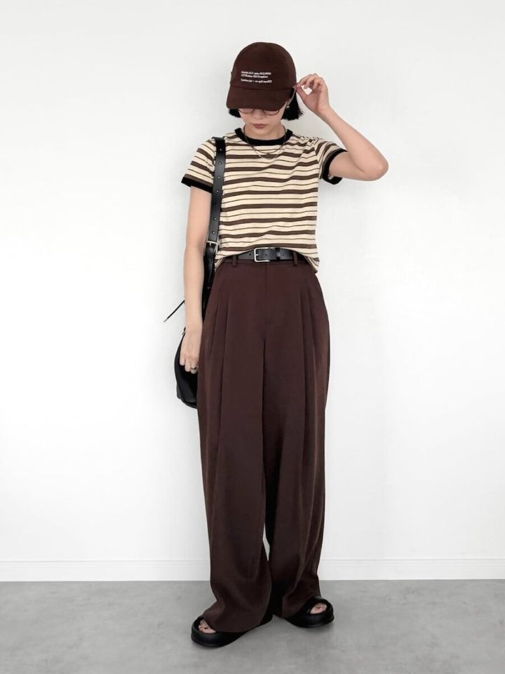ブラウンのワイドパンツとリンガーボーダーTシャツを着た女性がキャップを被り立っている