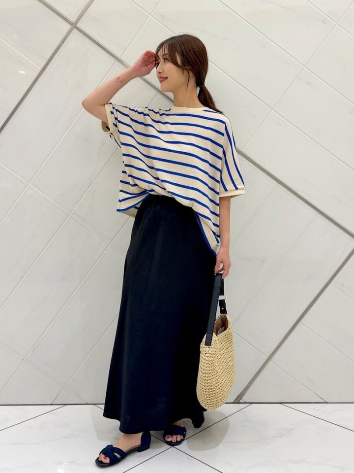 黒いフレアスカートとブルーのボーダーTシャツを着た女性がかごバッグを持ち横を向いて立っている