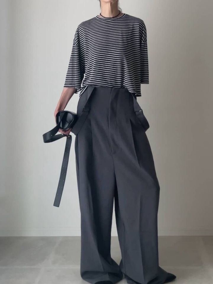 ダークグレーのワイドパンツと細ピッチボーダーTシャツを着た人物が黒いベルトを持っている
