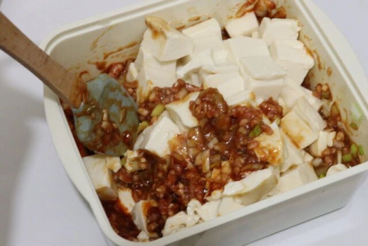 四角い容器の中で豆腐と麻婆豆腐の素を木製スプーンで混ぜている