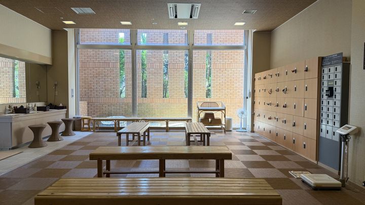 大きな窓を背景にロッカーや洗面台、長椅子が設置された脱衣所の様子