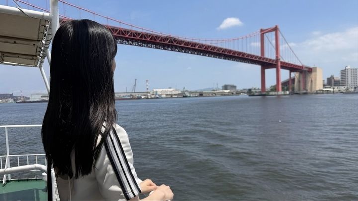 船上から真っ赤な若戸大橋と海を眺める女性の後ろ姿