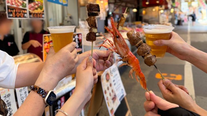 「九州まぐろ」の天然本まぐろ中トロ串、ボタン海老、冷えた生ビールを掲げる手
