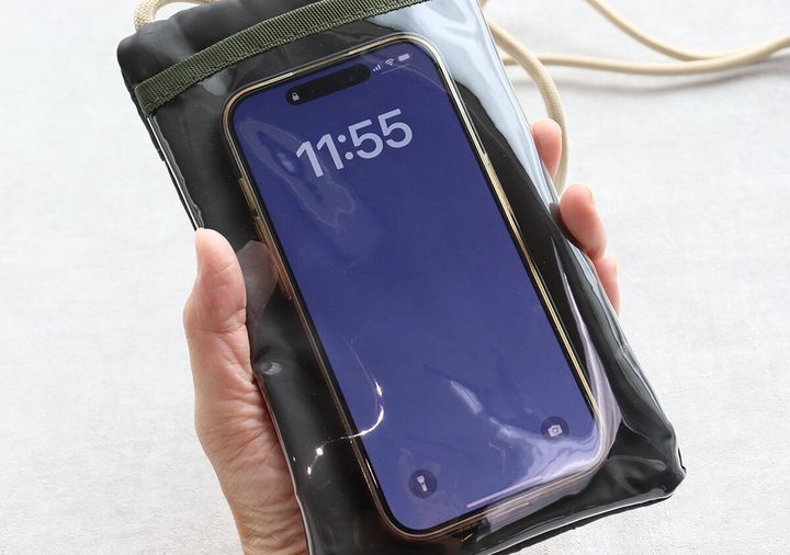 女性の手が、ショルダーポーチのクリアポケットに入ったスマートフォンを操作している