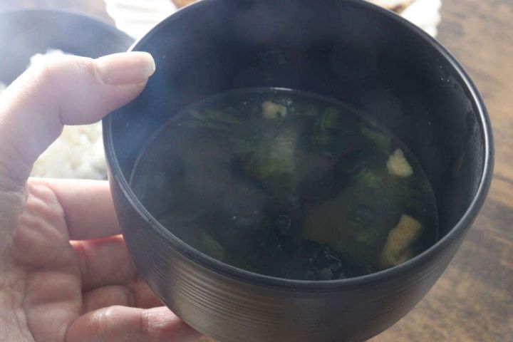 女性が味噌汁の入ったこげ茶色の汁椀を持つ