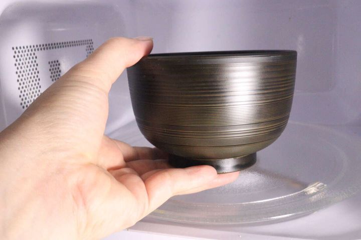 女性が汁椀を電子レンジのターンテーブルに置く