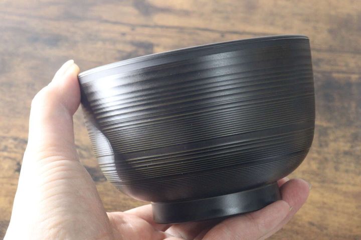 女性がこげ茶色の汁椀を手に持っている側面