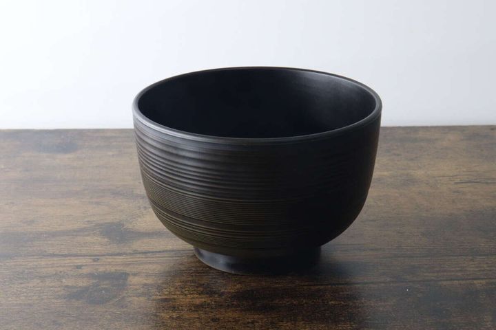 木目のテーブルに置かれたこげ茶色の汁椀