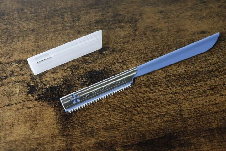 青い柄の貝印カミソリと半透明のキャップが木目調のテーブルに置かれている