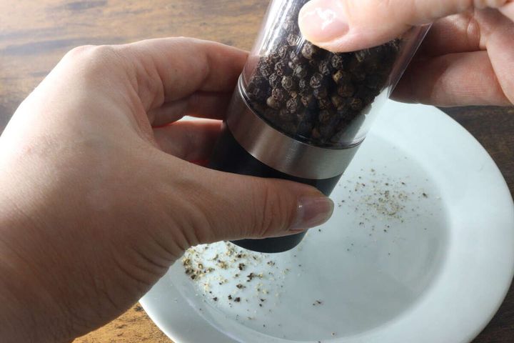 女性の手が2WAYグラインダーを回して白い皿に粒胡椒を挽いている