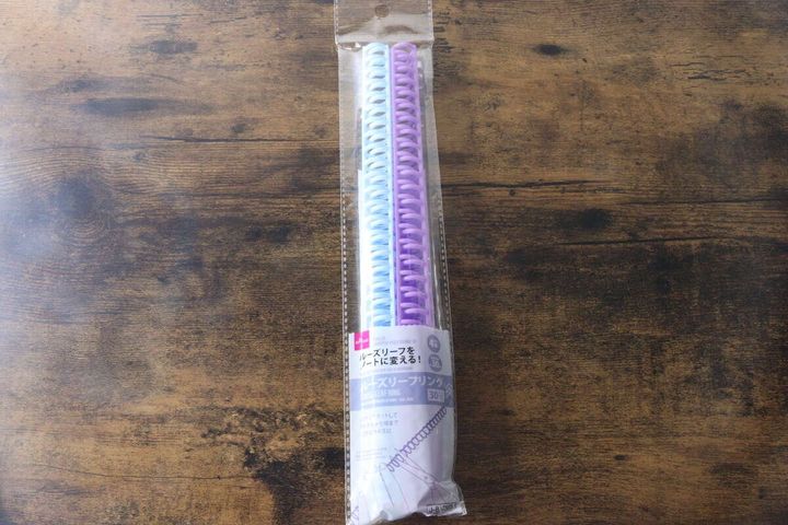パッケージに入った水色と紫色のルーズリーフリングが木目のテーブルに置かれている