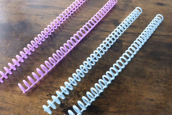 木目のテーブルに水色と紫色のルーズリーフリングが複数本並べられている