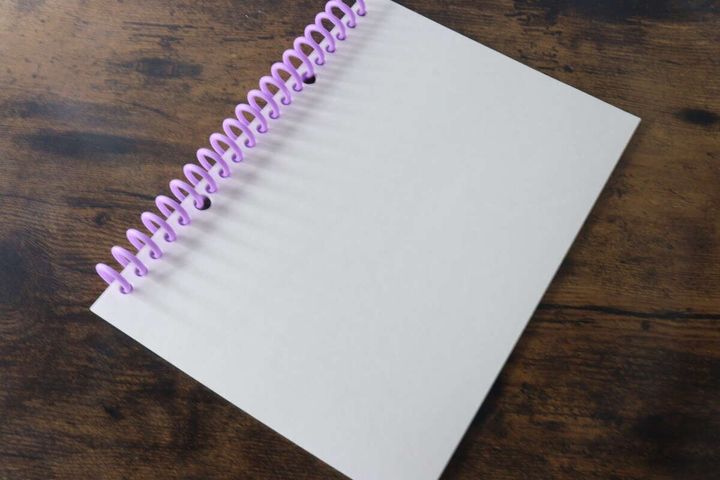 紫色のリングで綴じられた白いルーズリーフノートが木目のテーブルに置かれている