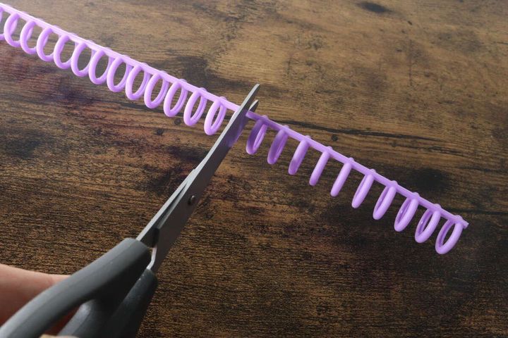 紫色のルーズリーフリングをハサミでカットしている手元