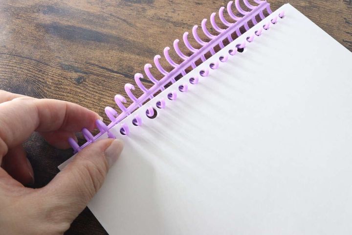 白いルーズリーフに紫色のリングを取り付けている手元
