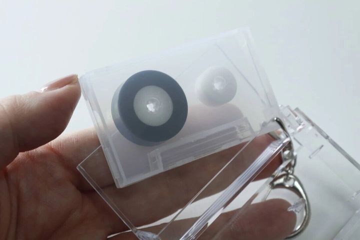 女性が透明なカセットテープ型キーホルダーを開き、中を見せている