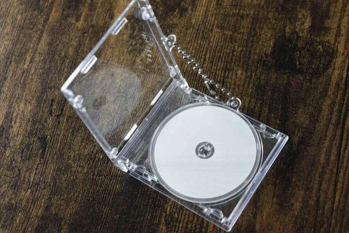 透明なCDケース型キーホルダーが開いており、中に白いCDが見える